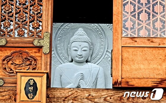 법당 안 건너편 통유리 바깥으로 조각 중인 부처님 모습. 그윽한 표정이 깊다.