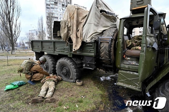 우크라이나 군 의무병이 25일(현지시간) 우크라이나 수도 키예프에서 공습대원들과 교전 중 총격을 당해 차량 옆에 누워 있는 우크라이나 군복을 입은 러시아 군인의 시신을 살펴보고 있다. © AFP=뉴스1