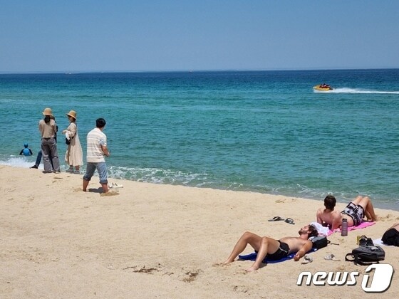 강원 강릉 경포해변에서 햇볕을 쬐고 있는 외국인 관광객 뒤로 바다에 모터보트가 지나가고 있다.(뉴스1 DB)