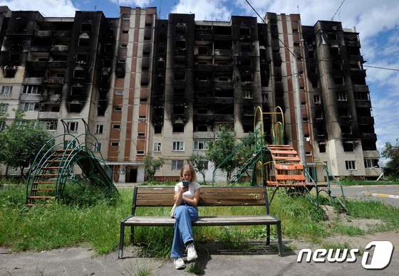 우크라이나 수도 키이우 인근 이르핀에서 러시아 군의 포격을 받아 시커멓게 그을린 아파트 앞 벤치서 소녀가 휴대폰을 보고 있다. © AFP=뉴스1 © News1 우동명 기자