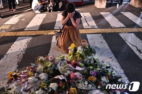 아베 신조(安倍晋三) 전 일본 총리가 총격 사망한 8일 사고 현장인 일본 나라 야마토사이다이지 역 외곽의 현장에서 한 여성이 꽃을 놓는 임시 기념비 앞에서 슬퍼하고 있다. © AFP=뉴스1 © News1 임세영 기자