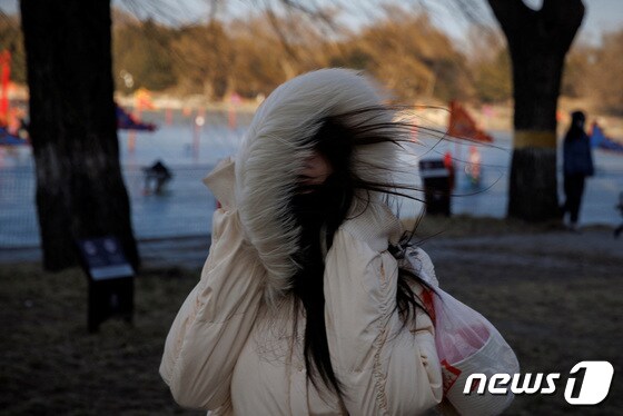 23일(현지시간) 중국 베이징에서 음력설 맞이 축제를 찾은 여성이 강하게 불어오는 바람을 모자로 막고 있다. © 로이터=뉴스1 © News1 권진영 기자