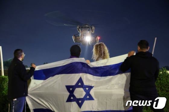 지난 28일(현지시간) 이스라엘 텔아비브 지역 라마트 간의 셰바 의료센터에 하마스와 이스라엘 간 인질-수감자 교환 거래로 풀려난 인질을 태운 헬리콥터가 도착하자 사람들이 이스라엘 국기를 흔들며 환영하는 모습이다.  2023.11.28/뉴스1 © 로이터=뉴스1 © News1 김민수 기자