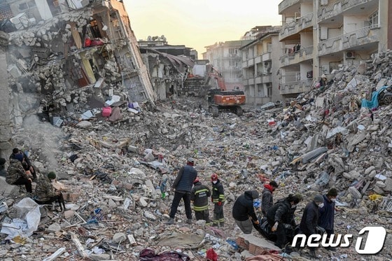 14일 (현지시간) 규모 7.8의 지진이 강타한 튀르키예 하타이에서 폭격을 맞은 듯한 붕괴된 건물의 잔해 주변서 주민들이 시신 백을 옮기고 있다. © AFP=뉴스1 © News1 우동명 기자