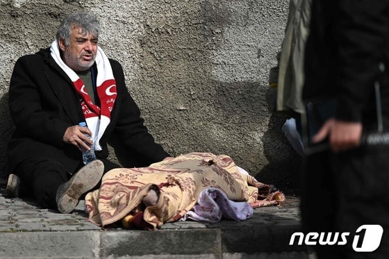 튀르키예 카라만마라슈의 건물 잔해 옆에서 한 남성이 담요를 씌운 아이 시신 옆에 앉아 있다. © AFP=뉴스1