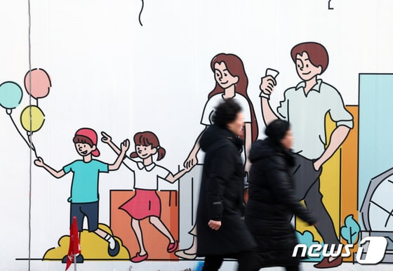 서울 도심의 공사장 가림막에 그려진 행복한 가족 그림 앞으로 시민들이 지나고 있다. 2024.1.29/뉴스1 © News1 박정호 기자