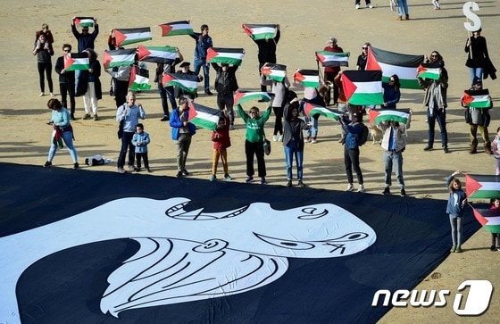 스페인 산세바스티안 지역의 라콘차 해변에 28일(현지시간) 피카소의 작품 '게르니카'가 펼쳐진 가운데 사람들이 팔레스타인 국기를 들고 있다. © AFP=뉴스1 © News1 정지윤 기자