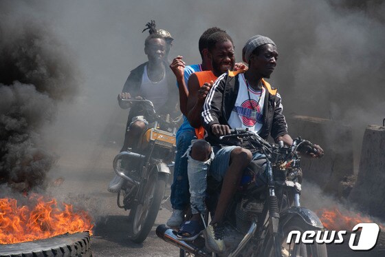 12일(현지시간) 아이티의 수도 포르토프랭스의 거리에서 타이어들이 불에 타며 연기를 내뿜고 있는 가운데 한 무리의 남성들이 오토바이를 타고 질주하고 있다. 2024.03.12 © AFP=뉴스1 © News1 정지윤 기자