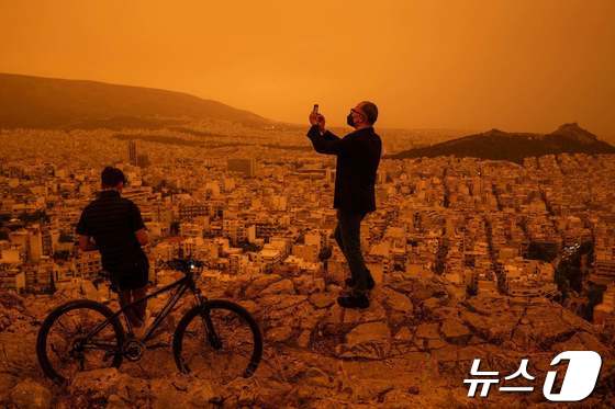 23일(현지시간) 남유럽 그리스 아테네 상공이 아프리카 사하라 사막에서 바람을 타고 넘어온 황색 모래로 뿌옇다. 한 남성이 아테네 투르코보니아 언덕에서 사진을 찍고 있다. 2024.04.23 © AFP=뉴스1 © News1 최종일 기자