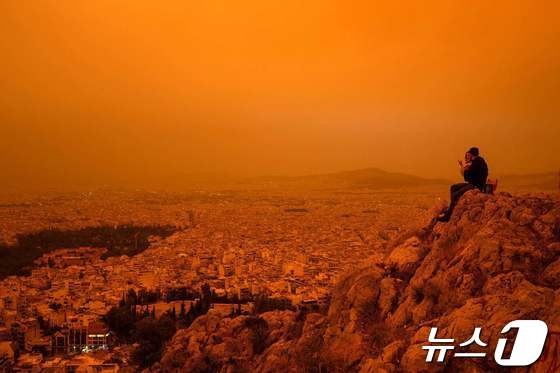 23일(현지시간) 남유럽 그리스 아테네 상공이 아프리카 사하라 사막에서 바람을 타고 넘어온 황색 모래로 뿌옇다. 한 커플이 아테네 투르코보니아 언덕에 앉아 있다. 2024.04.23 © AFP=뉴스1 © News1 최종일 기자