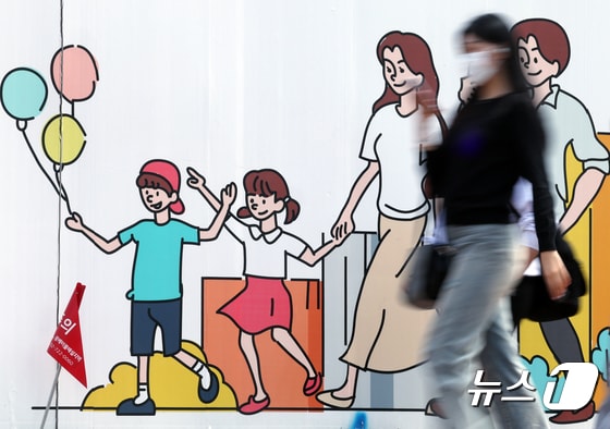 서울 도심의 공사장 가림막에 그려진 행복한 가족 그림 앞으로 시민이 지나고 있다. 2024.4.24/뉴스1 © News1 박정호 기자
