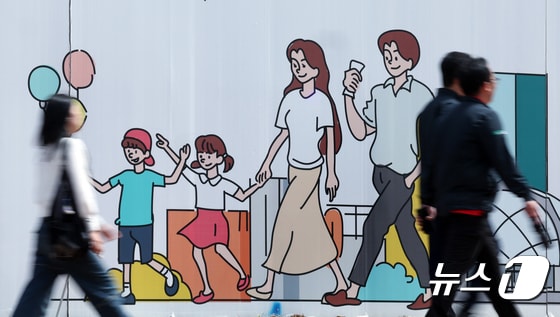 서울 도심의 공사장 가림막에 그려진 행복한 가족 그림 앞으로 시민이 지나고 있다. 2024.4.24/뉴스1 © News1 박정호 기자