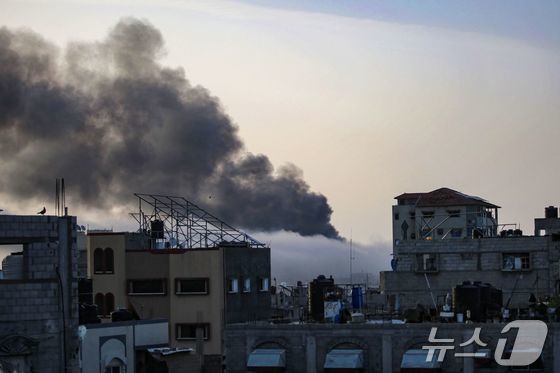 10일 동 트는 남부 가자 라파에 무너진 건물 사이로 이스라엘군 포격에 당한 건물에서 뿜어져 나오는 검은 연기가 하늘을 덮고 있다. 2024.05.10 © AFP=뉴스1 © News1 정지윤 기자