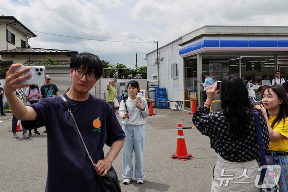 21일 일본 야마나시현 후지카와구치코 마을의 한 편의점에서 관광객이 후지산을 배경으로 사진을 찍고 있다. 2024.05.21/ © 로이터=뉴스1 © News1 권진영 기자