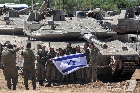 이스라엘군인들이 9일(현지시간) 이스라엘 국기를 펼쳐들고 남부 가자 접경지에 집결된 메르카바 전차앞에서 사진을 찍고 있다. 남다른 덩치의 메르카바 전차는 세계에서 방호력이 가장 우수한 탱크로 평가된다. 2024.05.09 © AFP=뉴스1 © News1 권진영기자