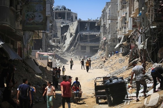 팔레스타인 시민들이 11일 이스라엘군 공습에 무너져 내린 가자 남부 칸유니스 건물들 사이를 지나고 있다 2024.06.11. © AFP=뉴스1 © News1 정지윤기자